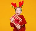 Happy little boy in red Christmas sweater and deer antlers holding Xmas gift against yellow wall Royalty Free Stock Photo