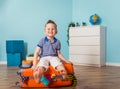 Happy little boy sitting on the suitcase. Child pretending to fly against blue background. Little tourists ready for