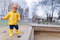 Happy little boy with teddy bear cap playing on playground at sandpit during autumn day.