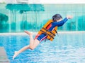 Happy little boy wearing orange life jacket has fun and enjoy jumping in the swimming pool. Royalty Free Stock Photo