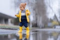 Happy little boy in yellow raincoat jumping in puddle after rain in autumn day.