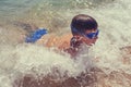 Happy little boy enjoying waves on beach in water