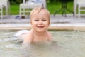 Happy little caucasian blond toddler boy swimming in wading pool on bright summer day at resort. Adorable baby enjoying outdoor Royalty Free Stock Photo