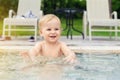 Happy little caucasian blond toddler boy swimming in wading pool on bright summer day at resort. Adorable baby enjoying outdoor Royalty Free Stock Photo