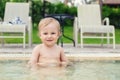 Happy little caucasian blond toddler boy swimming in wading pool on bright summer day at resort. Adorable baby enjoying outdoor Royalty Free Stock Photo