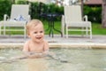 Happy little caucasian blond toddler boy swimming in wading pool on bright summer day at resort. Adorable baby enjoying outdoor Royalty Free Stock Photo