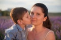 Happy little caucasian boy kissing his young smiling mother cheek on summer sunset flower field Royalty Free Stock Photo