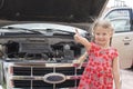 happy Little caucasian girl standing near the opened hood of the car, Royalty Free Stock Photo