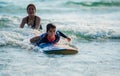 Happy little child boy learning to play surfboard from his mother with having fun and passion in sea on summer vacation at