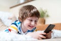 Happy little child boy playing online game, watching video on cellphone, lying on couch entertaining in living room Royalty Free Stock Photo