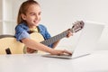 Cheerful girl with guitar using laptop