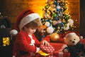 Happy little child dressed in winter clothing think about Santa near Christmas tree. Happy cute child in Santa hat with Royalty Free Stock Photo