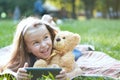 Happy little child girl looking in her mobile phone with her favorite teddy bear toy outdoors in summer park Royalty Free Stock Photo