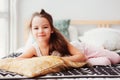 happy little child girl lying on her bed in the morning, waking up in comfortable room with modern bedlinen