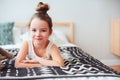 Happy little child girl lying on her bed in the morning, waking up in comfortable room with modern bedlinen