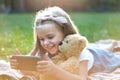 Happy little child girl playing her sellphone together with favorite teddy bear toy outdoors in summer park Royalty Free Stock Photo
