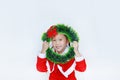 Happy little child girl in Santa costume with holding Christmas round wreath on her face on white background. Merry Christmas and Royalty Free Stock Photo