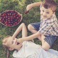 Happy little children lying near the tree with a basket of cherries at the day time. Royalty Free Stock Photo