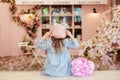 Happy little curly hair girl in dress and beret with bouquet of peonies sitting in street vintage cafe, view from back. Childhood