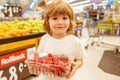 Happy little customer boy with strawberry, shopping at supermarket, grocery store. A boy is shopping in a supermarket