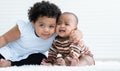 Happy Little cute African chubby kid girl hugging her crying newborn baby sister neck for comforting while sitting together Royalty Free Stock Photo