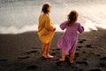 Happy little cute girls enjoying sunny day at the beach, standing on the coast and looking at the waves. Family summer vacation. Royalty Free Stock Photo