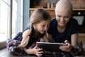 Happy little daughter kid and hairless cancer mom using tablet Royalty Free Stock Photo