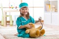 Happy little doctor girl examines teddy bear in nursery room at home