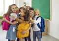 Happy little elementary school students hugging after meeting in school classroom.