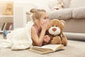 Happy little female child and her teddy bear reading book on the floor at home Royalty Free Stock Photo