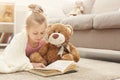 Happy little female child and her teddy bear reading book on the floor at home Royalty Free Stock Photo