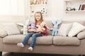 Happy little female child hugging her toy rabbits on sofa at home Royalty Free Stock Photo