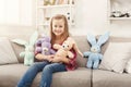 Happy little female child hugging her toy rabbits on sofa at home Royalty Free Stock Photo