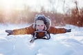 Happy little funny boy in warm winter clothes having fun on snow sledge, outdoors during snowfall