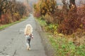 Happy little girl with blonde long hair running away on the road, back view. Walk in autumn time. Stylish fashion child outdoors. Royalty Free Stock Photo