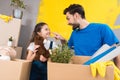 Happy little girl with box of plush toys looks at father which started repair in house.