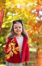 A happy little girl in a bright red coat and a white knitted sweater with a polka-dot headband plays in autumn park. Childhood.