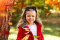 A happy little girl in a bright red coat and a white knitted sweater with a polka-dot headband plays in autumn park. Childhood.