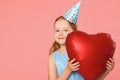 Happy little girl in a cap holds a big heart-shaped balloon. Portrait of a baby on a pink background. Copy space Royalty Free Stock Photo