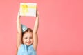 A happy little girl in a cap holds a box with a gift above her head. Portrait of a child on a pink coral background. Copy space Royalty Free Stock Photo