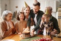 Happy little girl celebrating birthday with family at home, looking at cake with lit candles Royalty Free Stock Photo