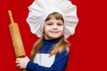 Happy little girl in chef uniform holds rolling pin isolated on light background. Kid chef Royalty Free Stock Photo