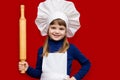 Happy little girl in chef uniform holds rolling pin isolated on light background. Kid chef Royalty Free Stock Photo