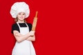 Happy little girl in chef uniform holds rolling pin isolated on red. Kid chef. Cooking Concept Royalty Free Stock Photo