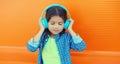 Happy little girl child in blue wireless headphones listening to music on orange background Royalty Free Stock Photo