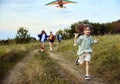 Happy little girl, child running with kite on trail in field. Spending time with parents and sister outdoors on warm Royalty Free Stock Photo