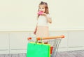 Happy little girl child with sweet caramel lollipop and shopping bags in trolley cart