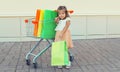 Happy little girl child with trolley cart and colorful shopping bags on city street Royalty Free Stock Photo