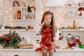 A happy little girl in the Christmas kitchen is sitting on the table with cookies in her hands and eating it Royalty Free Stock Photo