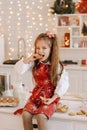 A happy little girl in the Christmas kitchen is sitting on the table with cookies in her hands and eating it Royalty Free Stock Photo